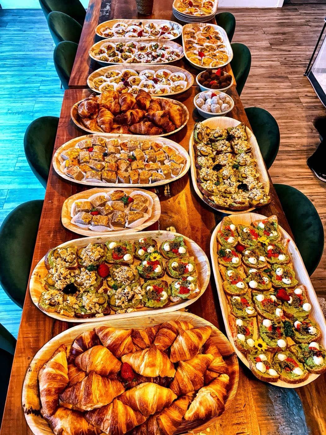 Long breakfast table at the office with croissants, avocado breads, egg muffins and banana bread