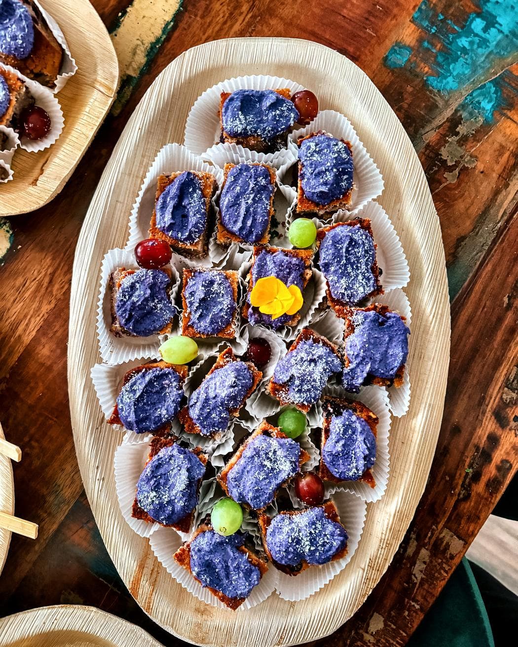 Platte mit Blaubeer-Kokos-Häppchen, Trauben und essbarer Blüte
