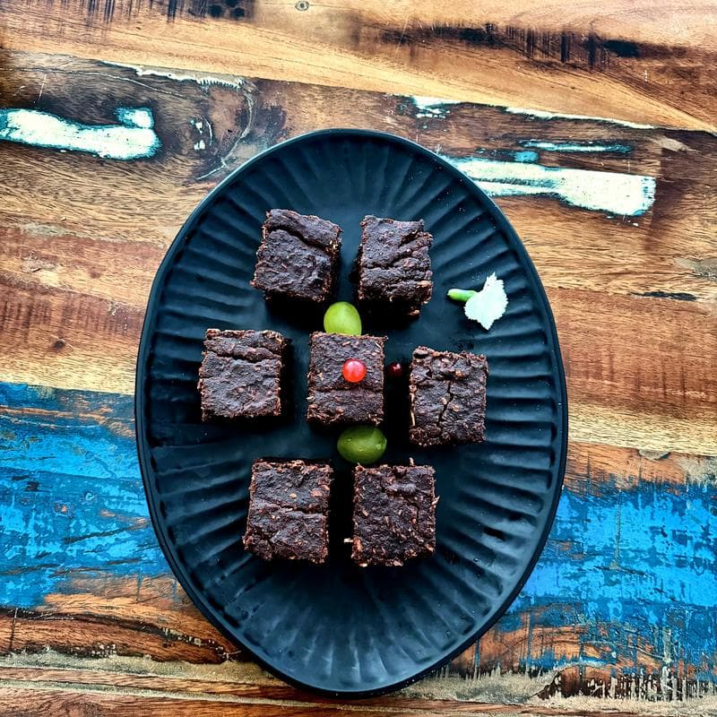Brownie-Häppchen auf schwarzer Platte mit Trauben und Johannisbeeren