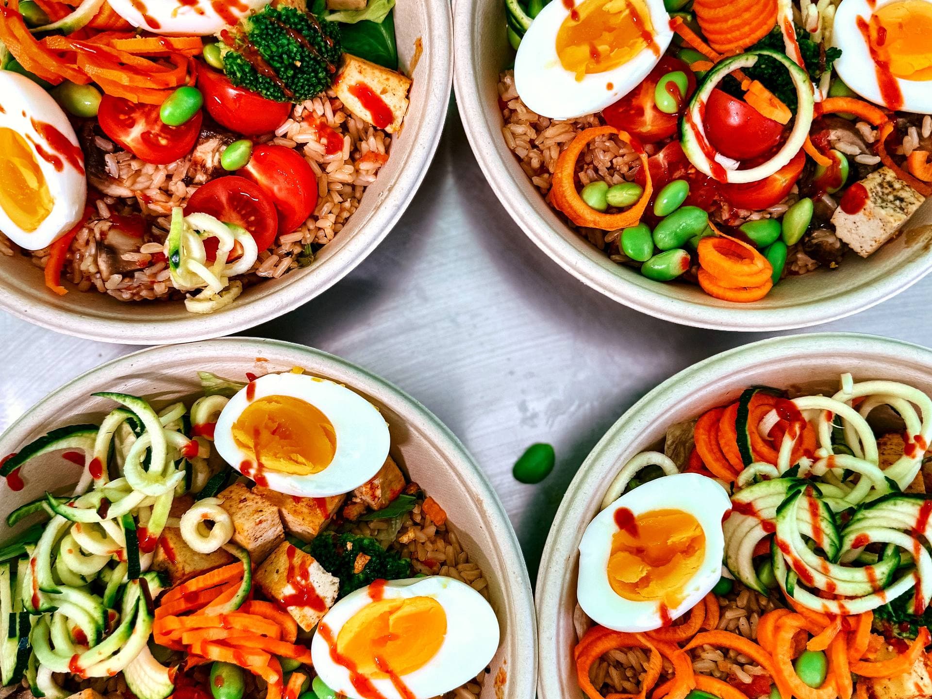 Vier AVOCAI Bowls mit braunem Reis, Zucchini-Nudeln, Tofu, Ei und Gemüse